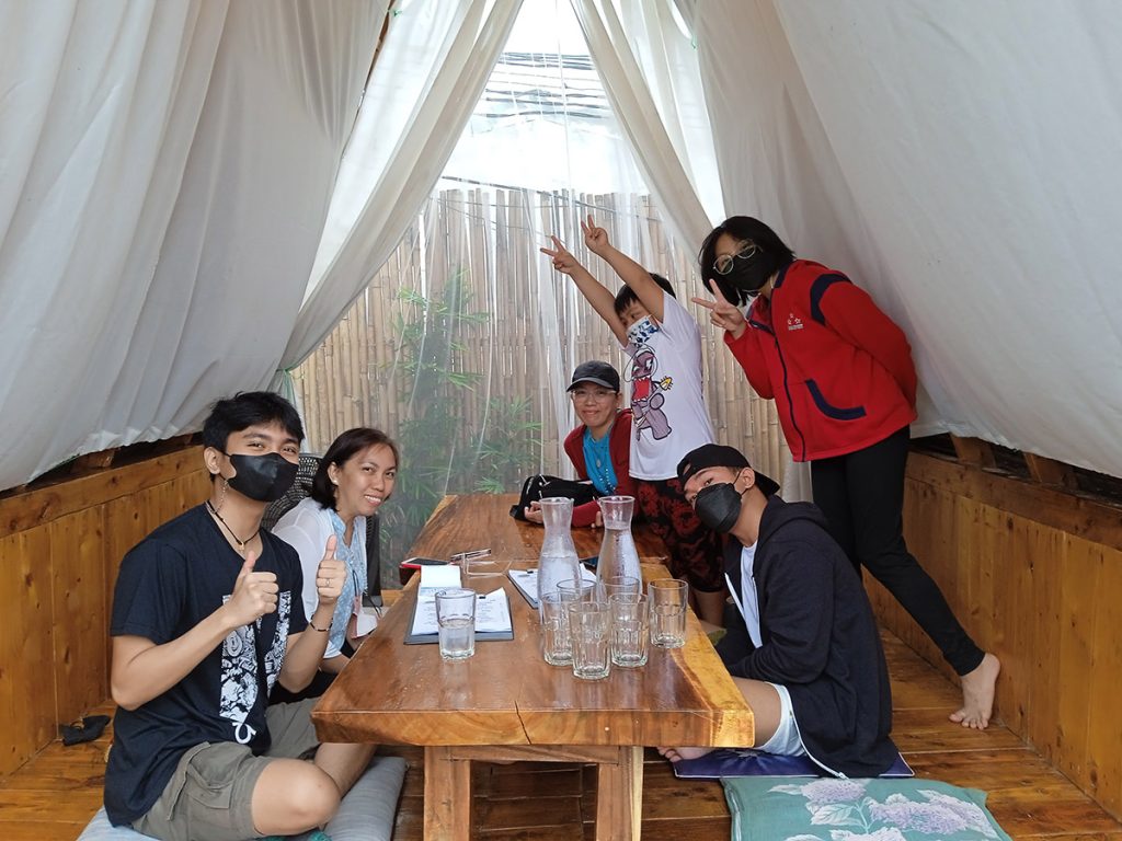 Family sitting around a table in a tent, engaged in conversation and enjoying each other's company.